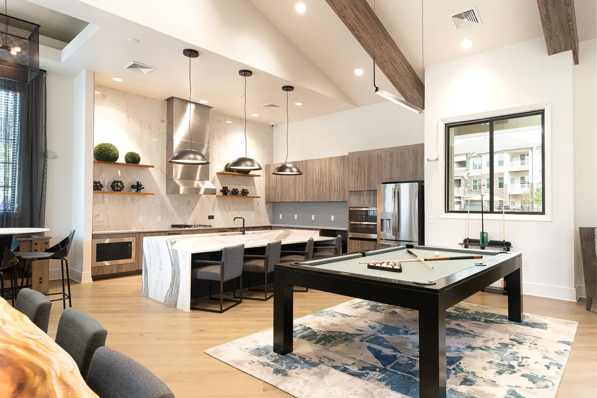 An open-plan area where a kitchen island flows naturally into a stylish dining space. The scene includes a pool table, large window, and ample seating, suggesting a lively area for cooking, dining, and social gatherings.