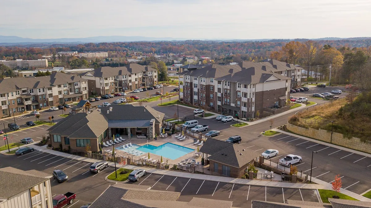 A sparkling swimming pool set amidst apartment buildings and a parking area, with residents relaxing and socializing outdoors. The scene radiates vibrancy and opportunity for leisure and community events.
