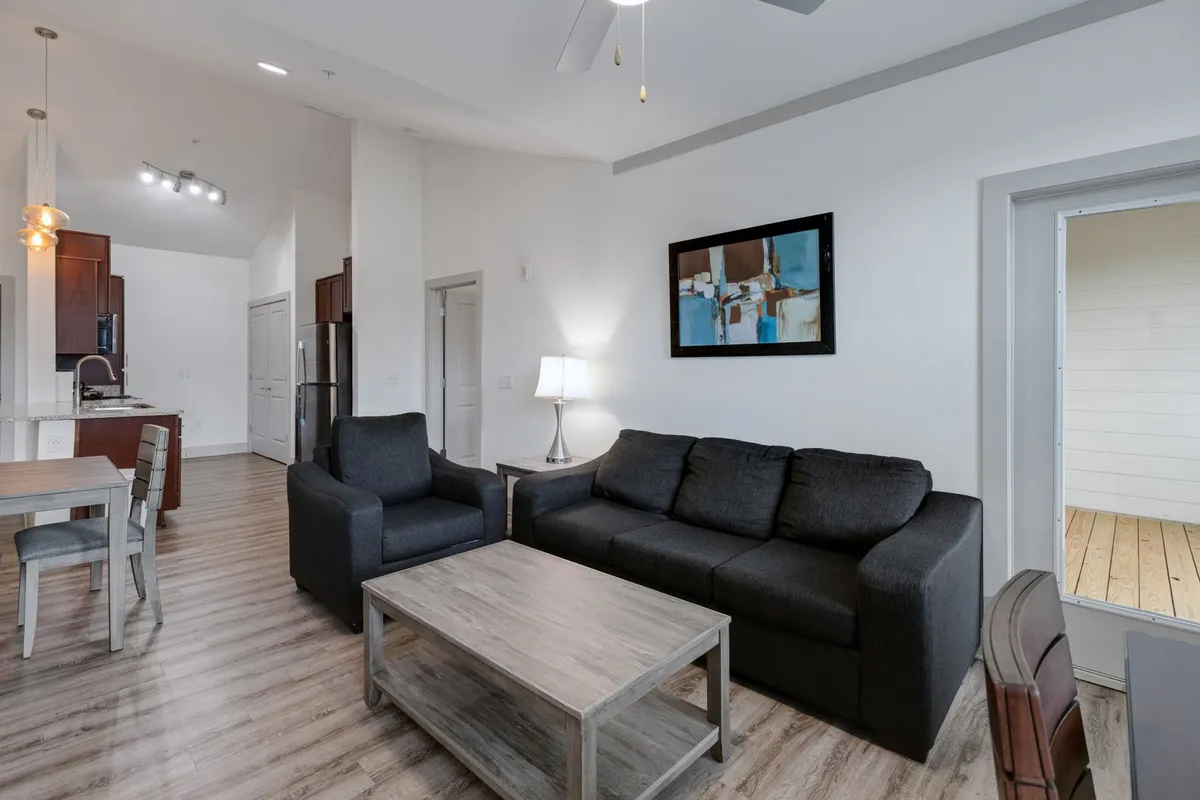 This image highlights a contemporary living room with a comfortable sofa, stylish artwork on the wall, and a dining table nearby. The space is filled with natural light, offering a seamless transition between lounging and dining areas. The overall design exudes warmth and a welcoming, homey feel.