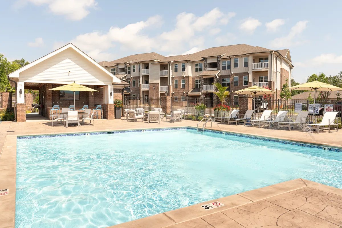 The image showcases a sparkling swimming pool surrounded by stylish lounge chairs and a cozy cabana, set against the backdrop of a modern apartment building. The scene is lively yet serene, hinting at activities like swimming, sunbathing, and socializing, all bathed in the warm glow of Tennessee's sunset.