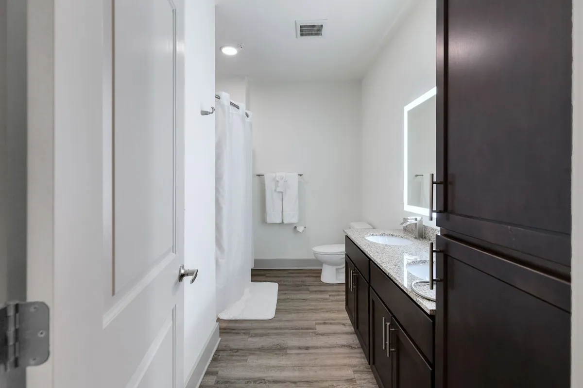 A modern bathroom featuring a double sink vanity topped with fresh towels, a large mirror that enhances the sense of space, and a glimpse of a sleek shower curtain. The light, clean color palette and uncluttered surfaces evoke a spa-like, refreshing ambiance.