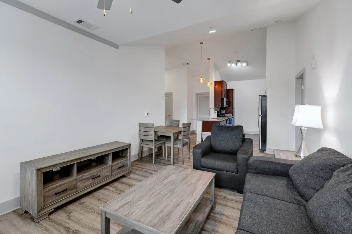 This image presents an open-concept space that combines a comfortable sofa, a modern coffee table, a dining table, and a kitchen area. The room is bathed in natural light, and the easy flow between spaces makes it perfect for both socializing and relaxing.