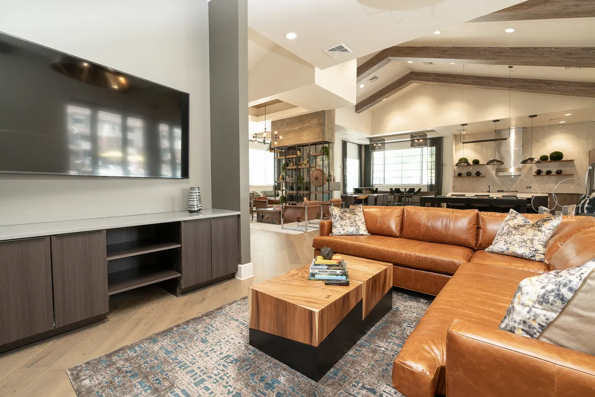 The image depicts a chic living room featuring a large leather sectional sofa, a stylish coffee table, and a wall-mounted television. The setup is perfect for both quiet evenings and lively gatherings, radiating a cozy, contemporary atmosphere.