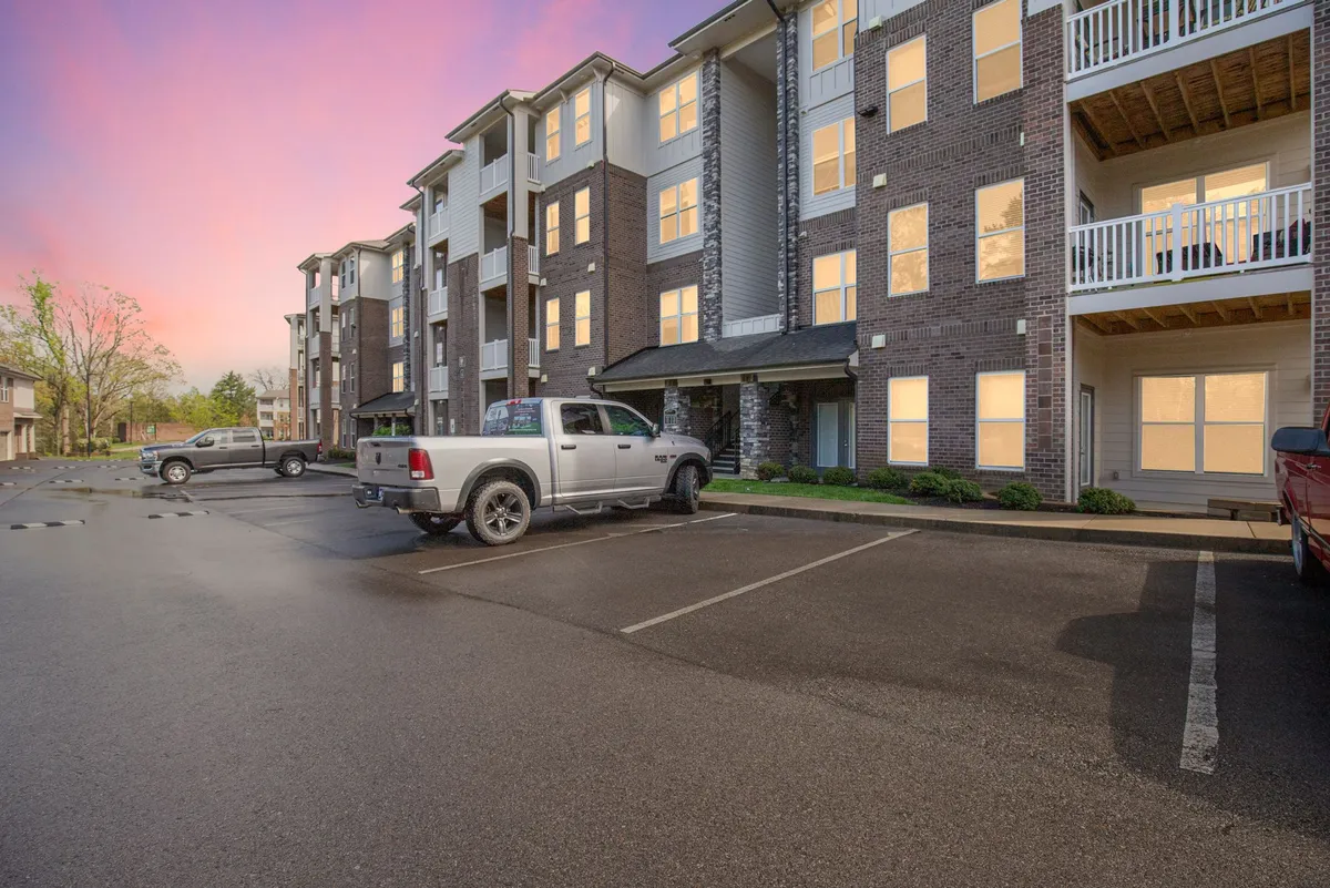 A modern apartment building is pictured in the golden light of sunset, with vehicles in the parking lot signaling easy access and convenience. Residents are seen socializing on balconies, illustrating a friendly, connected community.